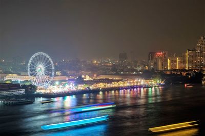 Illuminated ferris wheel in city against sky at night