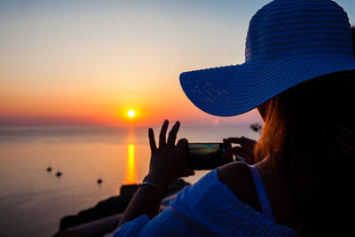 Rear view of woman photographing sea at sunset