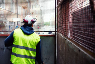 Rear view of construction worker looking through metal grate