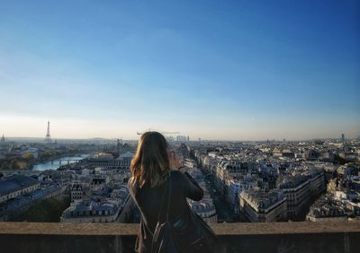 Rear view of woman standing by buildings in city against sky