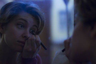 Reflection of young woman applying mascara on mirror