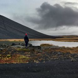 Rear view of person standing by lake against sky at hverfjall