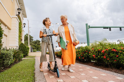 Portrait of happy senior women and granddaughter riding push scooter.