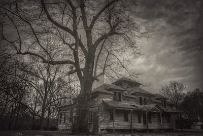 Low angle view of bare trees against cloudy sky