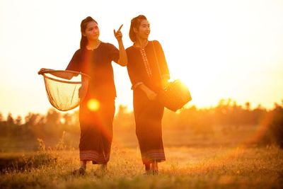 Woman standing on field against sky during sunset