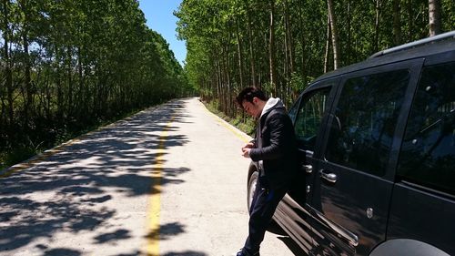 Side view of man leaning on car at roadside