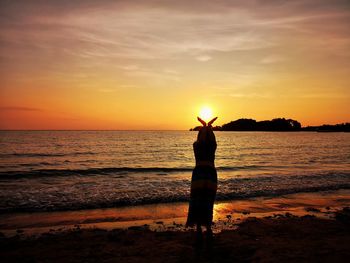 Silhouette person standing on beach against sky during sunset