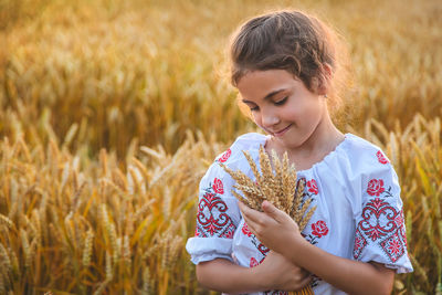 Cute girl holding wheat crops standing on field