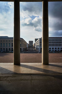 Buildings against cloudy sky seen through columns 