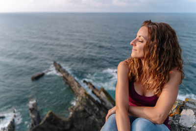 Side view of young woman sitting on sea against sky