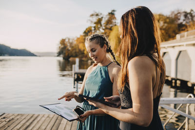 Young woman using mobile phone while standing by water