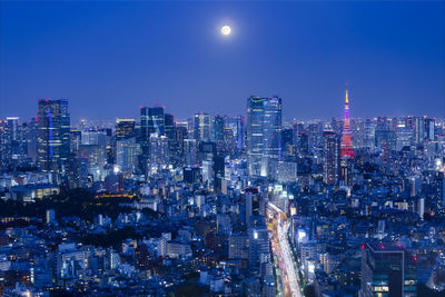 Illuminated cityscape against the full moon and clear blue sky