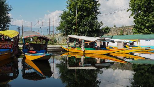 Boats moored by trees against sky