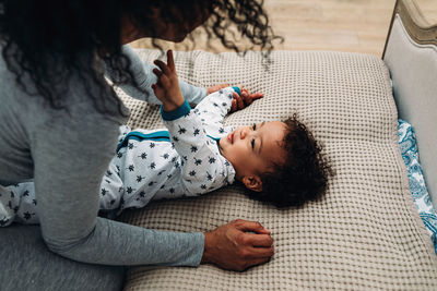 High angle view of baby boy looking at mother while lying on bed at home