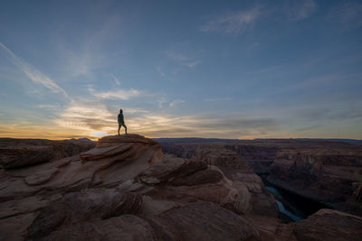 Man standing on rock against sky during sunset