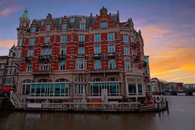 Building by river against sky during sunset