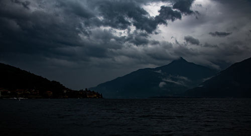 Scenic view of sea and mountains against storm clouds