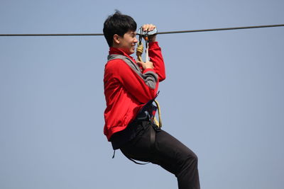 Man zip lining against clear sky