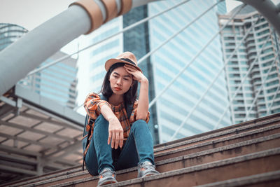 Portrait of young woman standing against railing in city
