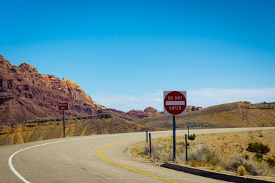 Road sign by mountains against blue sky