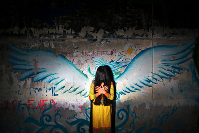 Rear view of woman standing against graffiti wall