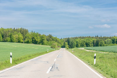 Empty road by trees against sky