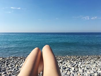 Low section of woman relaxing on beach against blue sky