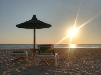 Chair on beach against sky during sunset