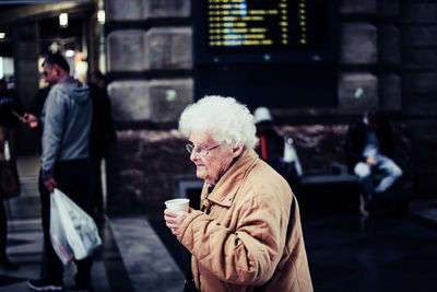 Side view of woman holding drink while standing on street