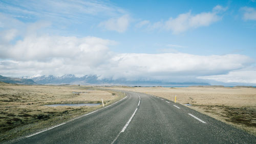 Empty road amidst landscape against cloudy sky