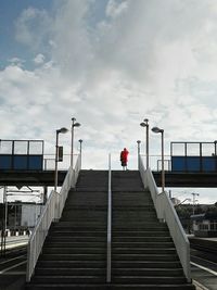 Rear view of woman standing on footbridge over railroad station against cloudy sky