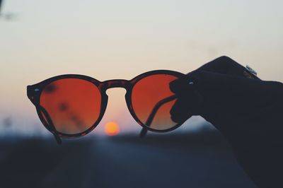 Close-up of sunglasses against sky during sunset