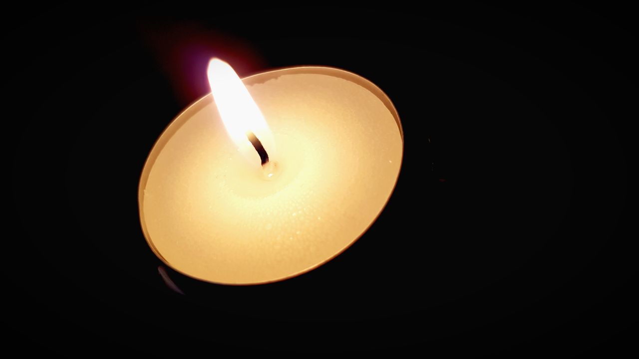 CLOSE-UP OF LIT TEA LIGHT CANDLE IN DARKROOM