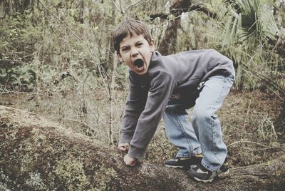 Full length side view of boy imitating gorilla in forest