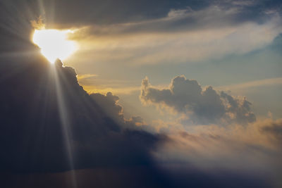 Low angle view of sunlight streaming through clouds during sunset