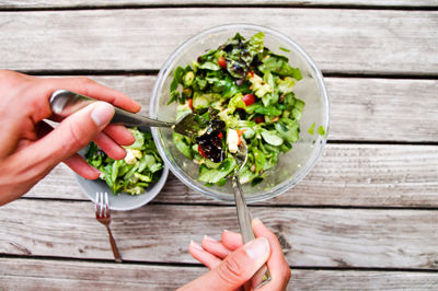 Directly above shot of hand mixing salad in bowl on table