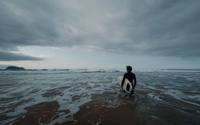 Rear view of man with surfboard in sea against sky