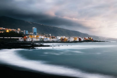 City at waterfront against cloudy sky