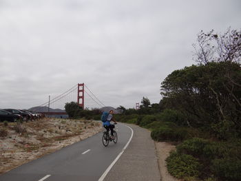 Woman riding bicycle on road against golden gate bridge