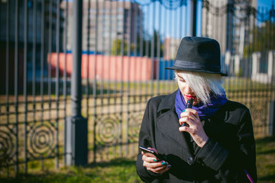 Young woman using mobile phone while smoking at park
