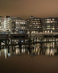 Illuminated buildings by river against sky at night