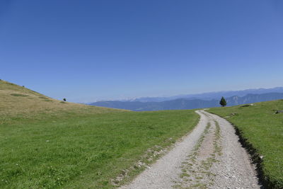 Road amidst field against clear sky