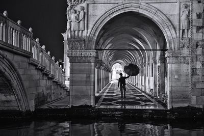 Rear view full length of man with umbrella in corridor at san marco during night