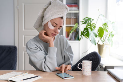 Woman with eye patches using mobile phone at home