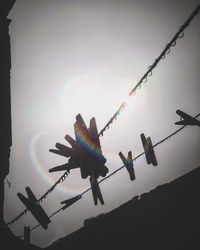 Low angle view of silhouette clothespins hanging from wet string against sky on sunny day