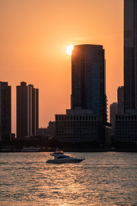 Sea by buildings against sky during sunset