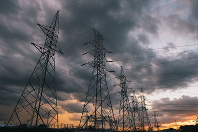 Low angle view of silhouette electricity pylon against dramatic sky