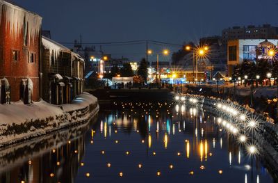 Illuminated buildings by river against sky in city at night