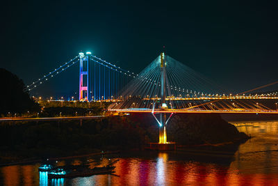 Illuminated suspension bridge over river at night