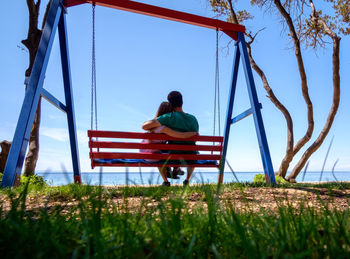 Rear view of girl sitting on grass against clear sky